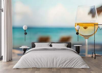  A glass of wine on a sandy beach, near the ocean; a sunny day features a straw umbrella Wall mural