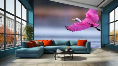  A pink bird flies over a tranquil body of water, its yellow beak contrasting against the background of a solitary tree Wall mural