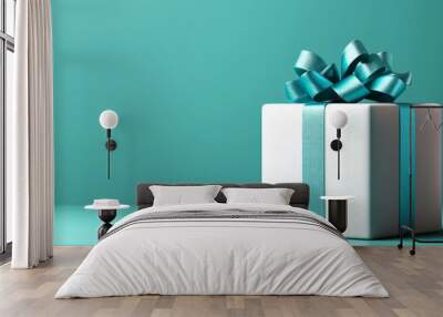  A white gift box, adorned with a blue ribbon and bow atop, situated against a teal backdrop Wall mural