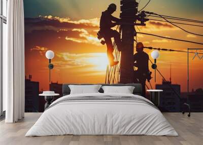 Silhouette of linemen working on an electric pole against a vibrant sunset, showcasing teamwork and dedication in the utility industry. Wall mural