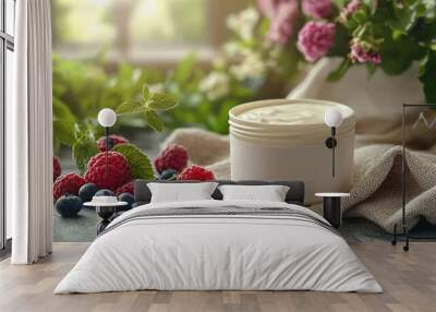 A jar of cream sits on a table with a bunch of raspberries and blueberries Wall mural