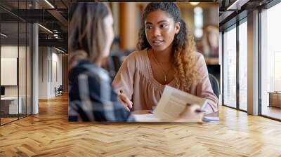 Two women are sitting at a table, one of them writing something down Wall mural