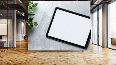 Modern tablet computer with blank white screen on a minimalist textured surface alongside a vibrant green plant. Wall mural