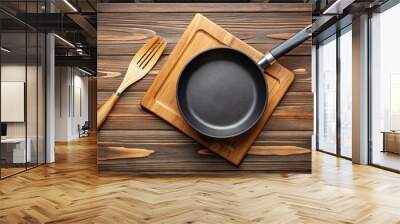 Photo image of a solitary non-stick skillet resting on a wooden cutting board, with a single utensil lying beside it. Wall mural