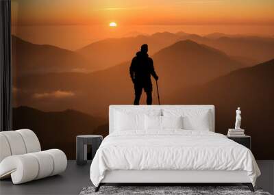 Silhouette of a man with a backpack and trekking poles on the top of the mountain at sunrise. Wall mural