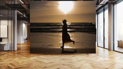 Women enjoying a run on the beach by the sea at sunset Wall mural