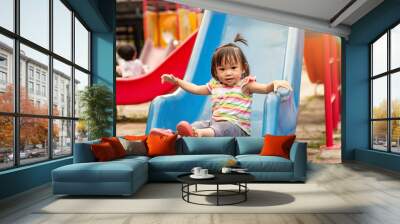 Asian child girl playing a slider toy at the playground. Happy Baby aged 2 years old. Wall mural