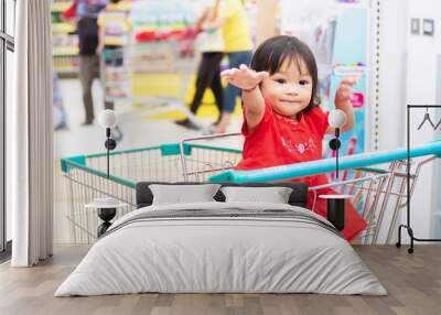 Portrait image of baby 1-2 years old. Happy Asian child girl sitting in a cart shopping at the supermarket. Wall mural