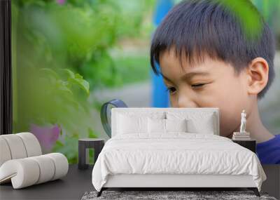 Portrait of happy Asian child boy holding and looking with magnifying glass on the flower tree and green grass field floor. Adventure, explorer and learning kid. Childhood 5-6 years old. Wall mural