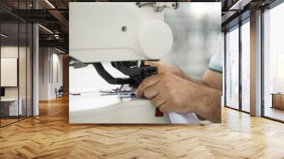 seamstress male on a sewing machine makes a shirt in the sewing workshop. the man on the machine sews the collar and cuffs Wall mural