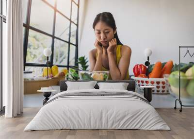 A young Asian woman who eats vegetable salad every day is bored with vegetables. Unhappy women is on dieting time looking vegetable on the fork. girl do not want to eat vegetables and dislike taste. Wall mural