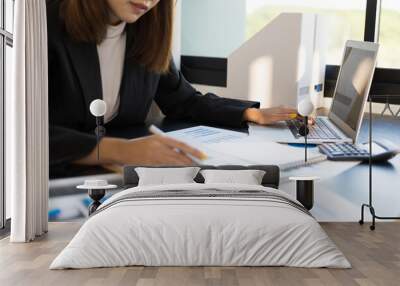 Business woman working on an audit using laptop at her desk in the office. Wall mural