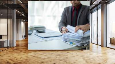 A man is sitting at a desk with a pile of papers in front of him Wall mural