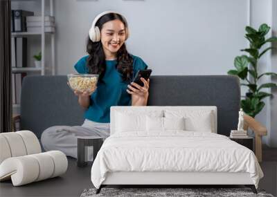 A woman is sitting on a couch, holding a bowl of popcorn and a cell phone Wall mural