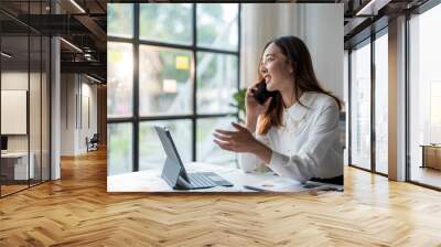 Businesswoman is negotiating with a client on the phone while analyzing a sales chart on a tablet Wall mural