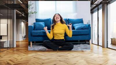 Happy young woman celebrating success while using smartphone at home Wall mural