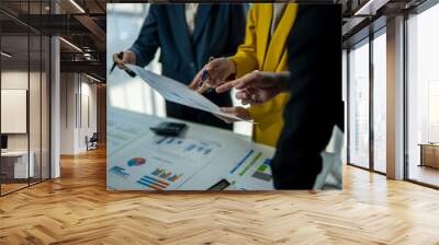 Three people are looking at a piece of paper with graphs on it. They are discussing the data and making decisions based on it Wall mural