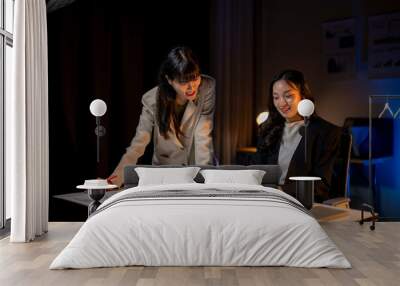 Two young businesswomen working late and brainstorming over financial charts Wall mural