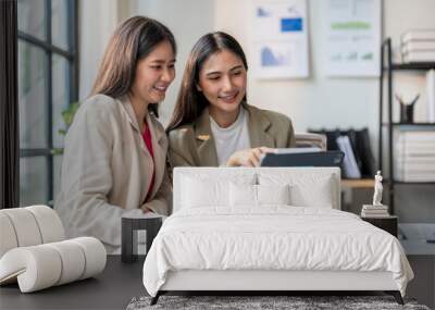 Two young businesswomen working together using laptop in office Wall mural