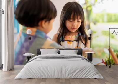 Two young children baking together in kitchen wearing aprons Wall mural