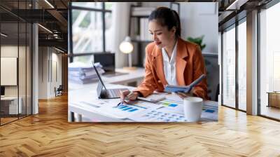 Young asian businesswoman analyzing financial chart using digital tablet and calculator in office Wall mural