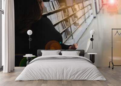 Young beautiful lady reading book at left side of blurred bookshelf,in library, Wall mural