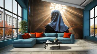 A nun stands in a church, her face hidden by her veil. The light from the stained glass window shines down on her, creating a halo around her head. She is wearing a brown robe. Wall mural