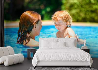 A woman teaches a baby to float on the water and swim. Summer outdoor fun in the pool in the villa. Happy child is having fun. Family happiness. Mom and daughter in the pool Wall mural