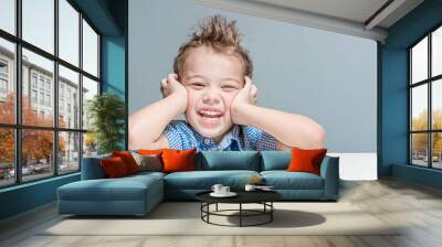 Cute smiling boy sitting at the table on a gray background in the studio. Isolated. Wall mural