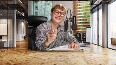 Cheerful asian man podcaster sitting front of microphone and laptop at his home studio. Wall mural