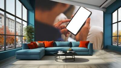 Over shoulder close up view, man holding smartphone with mockup white blank display, empty screen for advertise or text message. Wall mural