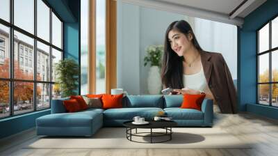 Satisfied asian young woman relaxing at her workplace and looking through the window at office. Wall mural