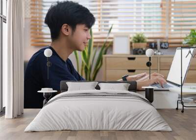 Smiling handsome asian man sitting on floor in living room and using laptop computer. Wall mural