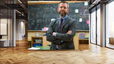 A teacher in a classroom, standing with arms crossed in front of a chalkboard, professional and educational environment Wall mural