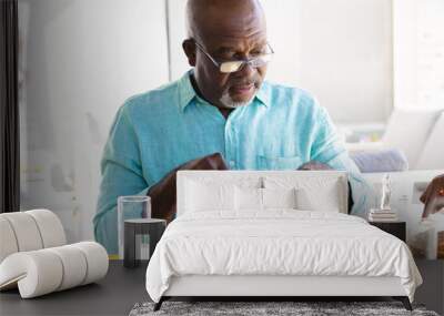 African american bald senior man wearing eyeglasses eating fruits for lunch on dining table at home Wall mural