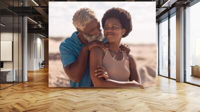 African american bearded senior man with hands on mature woman's shoulders at beach against sky Wall mural