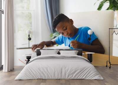 African american boy sitting at table in living room, doing homework Wall mural