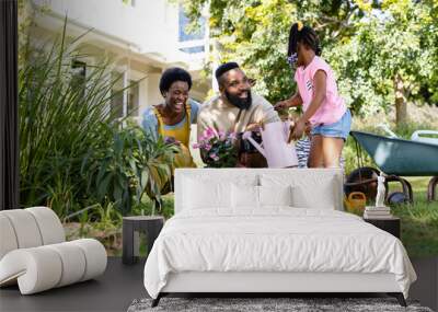 African american cheerful parents with children planting and watering flowers on field in backyard Wall mural