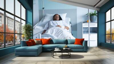 African american female patient lying on bed and looking away in hospital room Wall mural