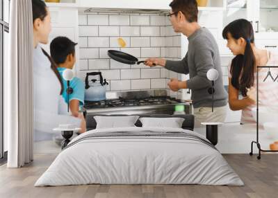 Asian mother, son and daughter watching father tossing pancake for breakfast in kitchen Wall mural