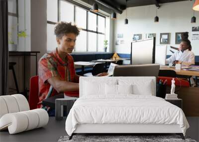 Biracial young businessman using laptop at desk in creative office Wall mural