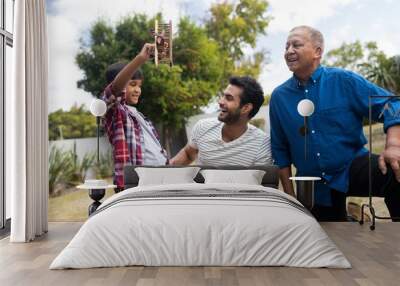 Boy showing toy airplane to father crouching by senior man Wall mural