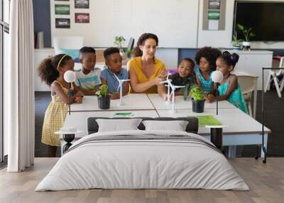 Caucasian young female teacher explaining windmill model to african american elementary students Wall mural