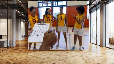 Focused biracial female basketball players with male coach discussing game plan on clipboard at gym Wall mural