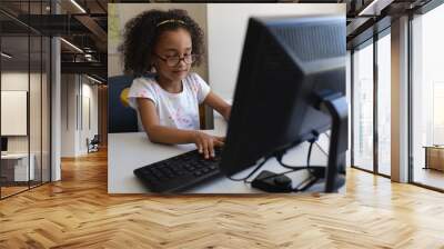 Front view little schoolgirl using desktop pc at desk in Wall mural