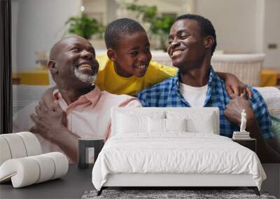 Happy african american boy with father and grandfather sitting on sofa at home Wall mural