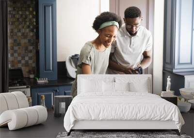 Happy african american couple preparing meal together using tablet in kitchen Wall mural