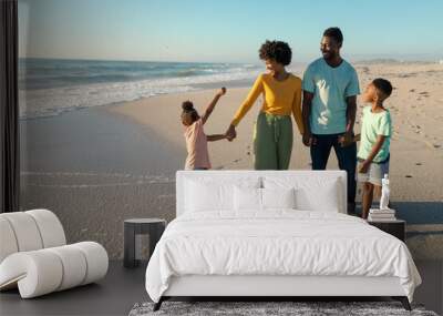 Happy african american family enjoying sunny day at beach against blue sky Wall mural