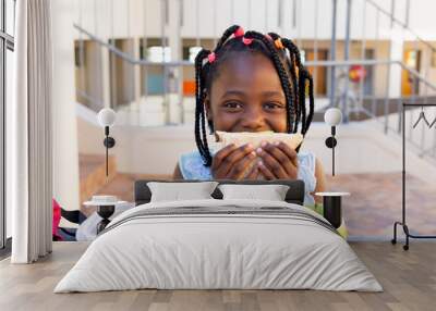 Happy african american schoolgirl having healthy lunch eating sandwich at elementary school Wall mural