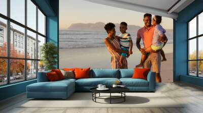 Happy african american young parents carrying son and daughter while standing against sea and sky Wall mural